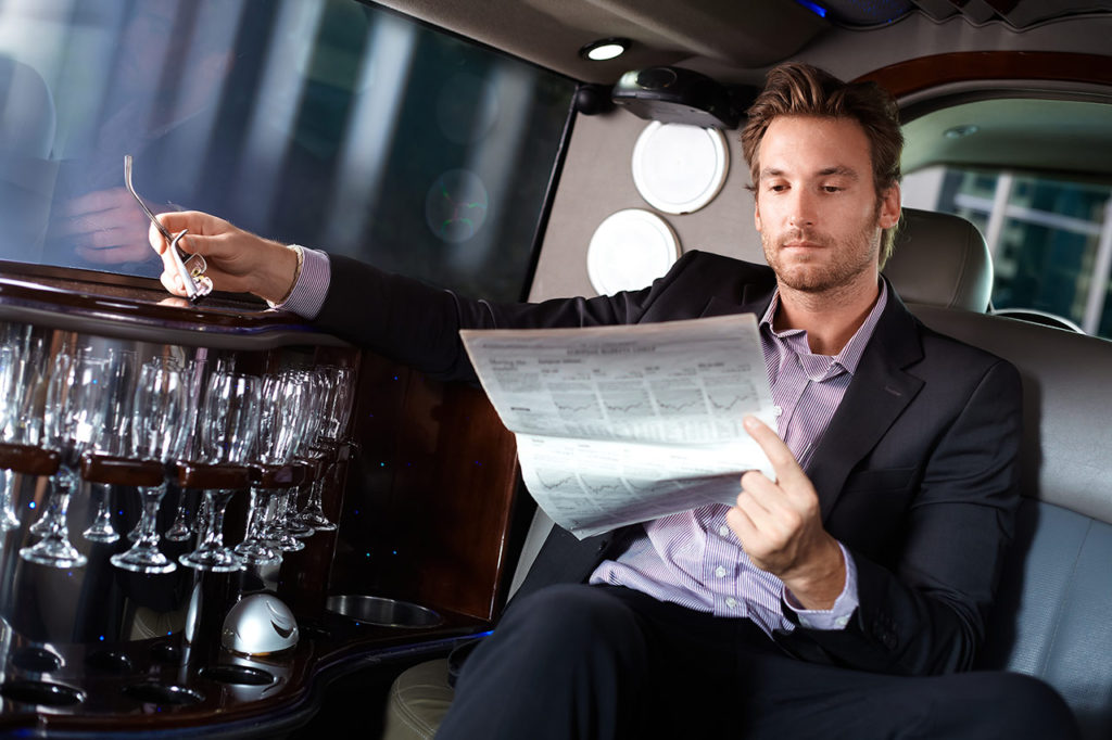 A man sitting in the back of a limo reading paper.