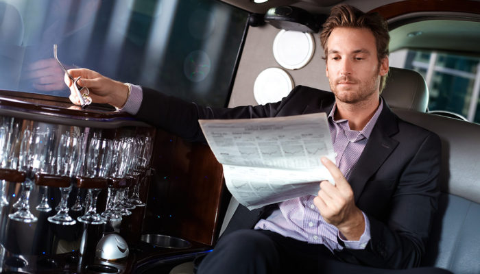 A man sitting in the back of a limo reading paper.