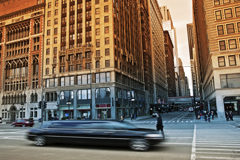A car driving down the street in front of tall buildings.