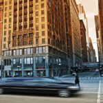 A car driving down the street in front of tall buildings.