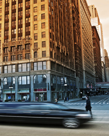 A car driving down the street in front of tall buildings.