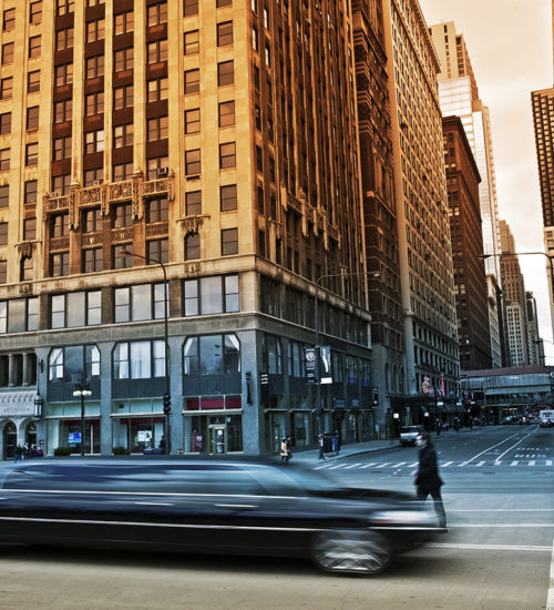 A car driving down the street in front of tall buildings.