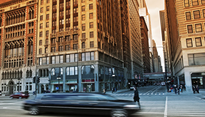 A car driving down the street in front of tall buildings.