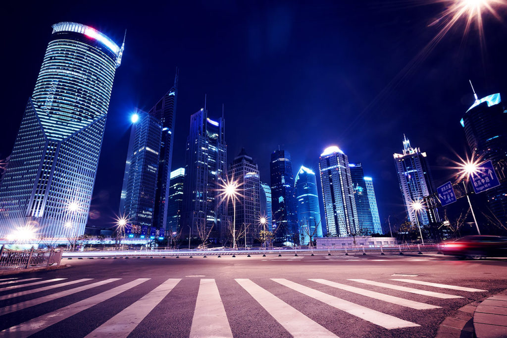 A city street with lights and skyscrapers at night.