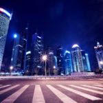 A city street with lights and skyscrapers at night.