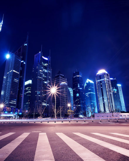 A city street with lights and skyscrapers at night.