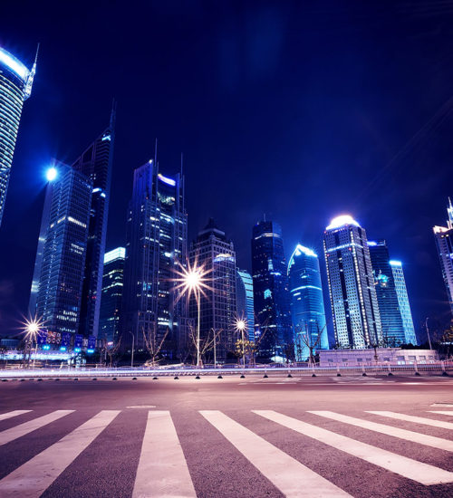 A city street with lights and skyscrapers at night.