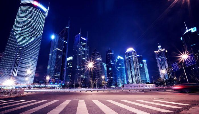 A city street with lights and skyscrapers at night.