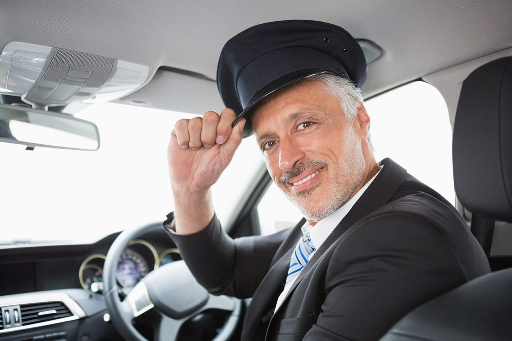 A man in a suit and hat sitting inside of a car.