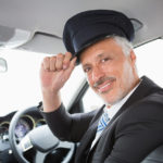 A man in a suit and hat sitting inside of a car.