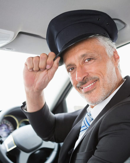 A man in a suit and hat sitting inside of a car.