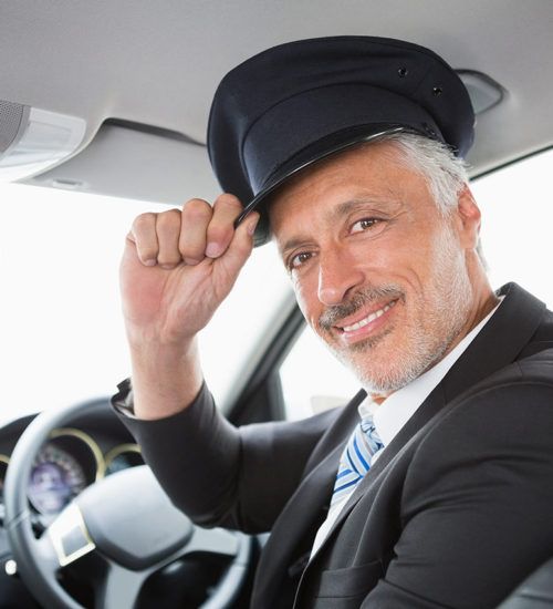 A man in a suit and hat sitting inside of a car.