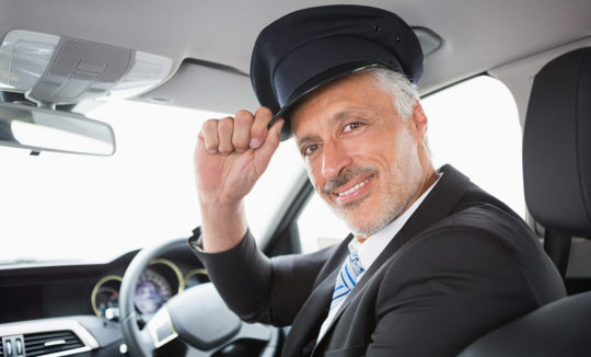 A man in a suit and hat sitting inside of a car.