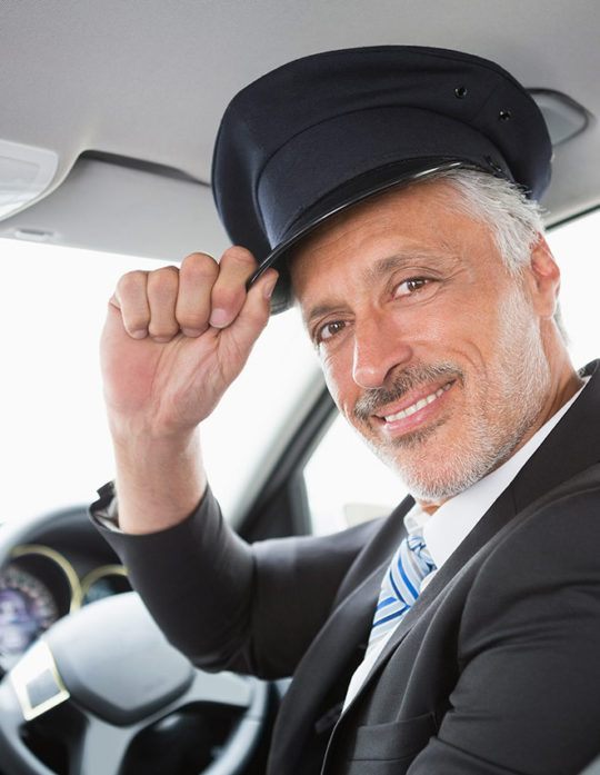 A man in a suit and hat sitting inside of a car.