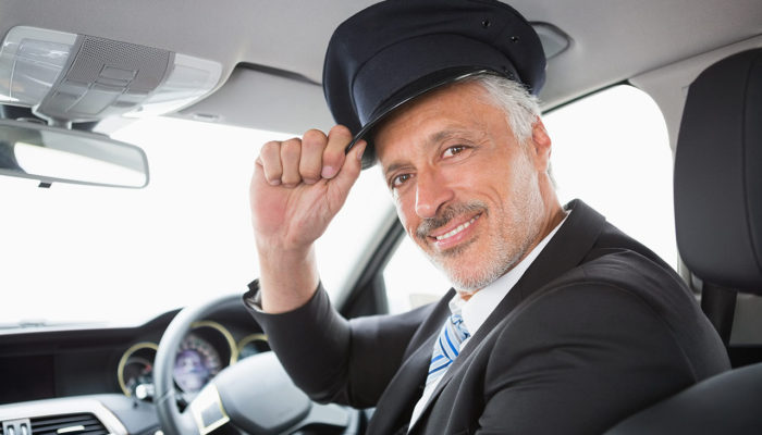 A man in a suit and hat sitting inside of a car.