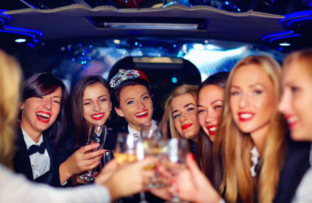 A group of women holding wine glasses in the back of a limo.