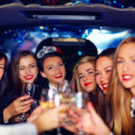 A group of women holding wine glasses in the back of a limo.