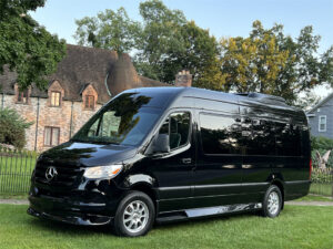 Black Mercedes-Benz Sprinter van parked near a stone building and trees.